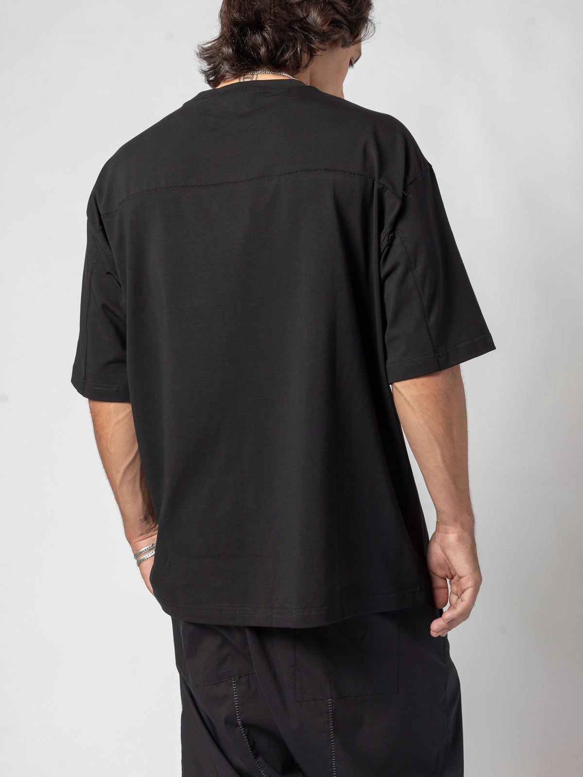 AITO Oversized Cotton T-Shirt in Black - back three-quarter of the torso, head turned over the shoulder, cropped above the hem