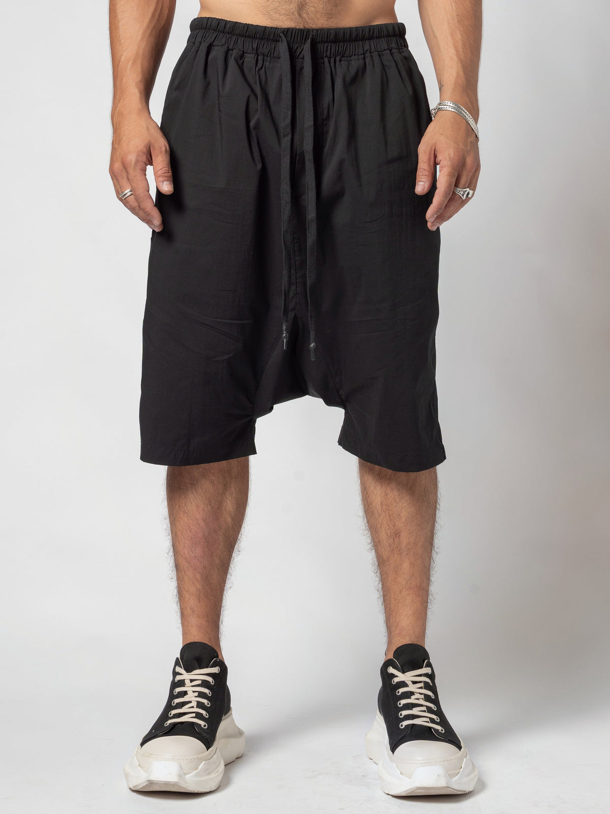 AITO Drop-Crotch Cotton Shorts in Black - front view, full length from the waist to the shoes, hands resting at the sides and the drawcord hanging down the centre