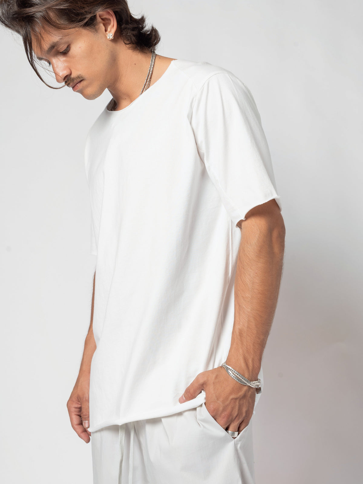 AITO Scar Stitch Cotton T-Shirt in White - front view of the torso, head turned down and away, both hands in the pockets