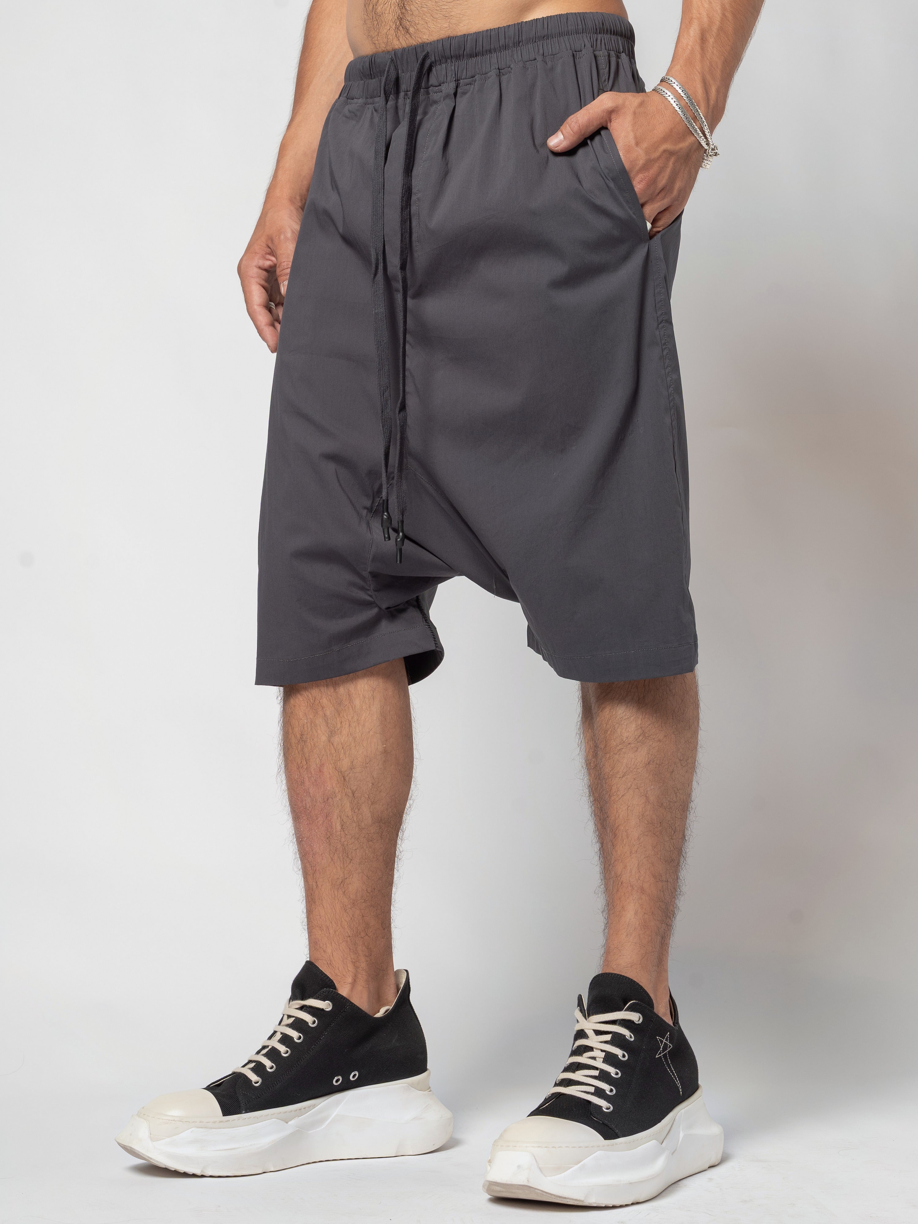 AITO Drop-Crotch Cotton Shorts in Dark Grey - full-length front view with a hand in the pocket and the drawcord running down the front
