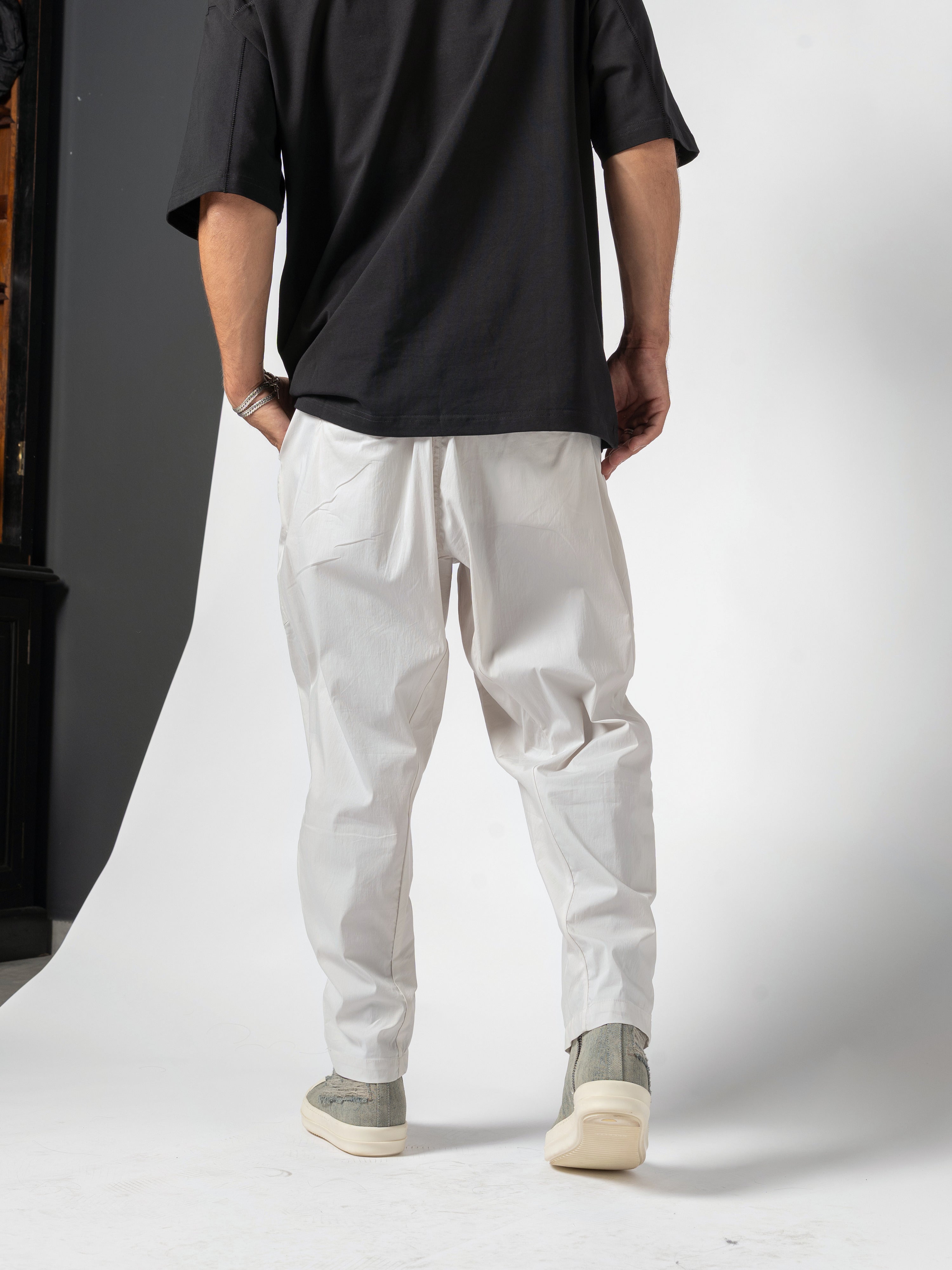 AITO Pleated Drop-Crotch Pants in Off White - back view worn with the black tee, a hand tucked into the back pocket, waistband down to the shoes