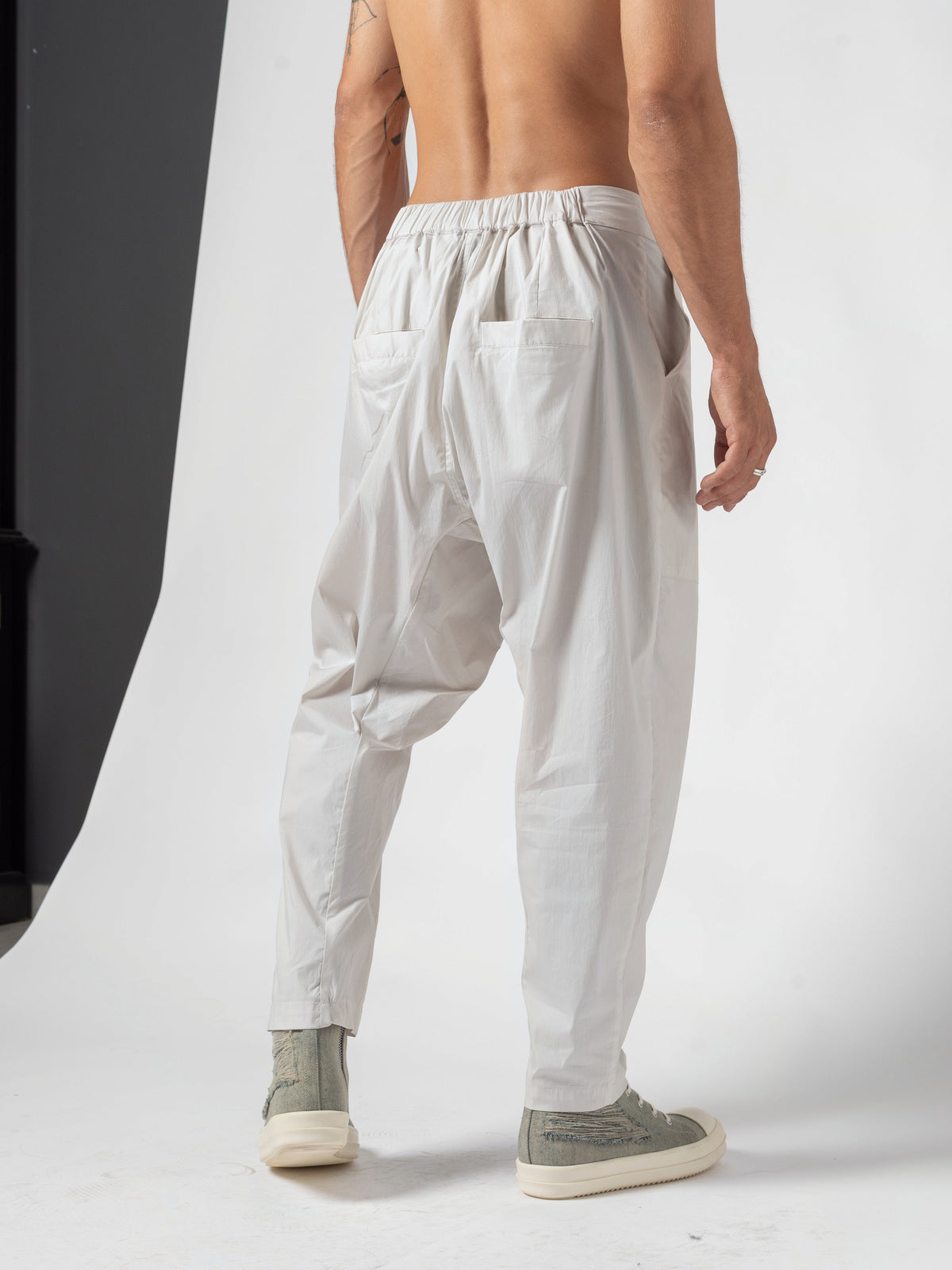AITO Pleated Drop-Crotch Pants in Off White - back view with the torso twisted the other way, both arms hanging clear of the pockets