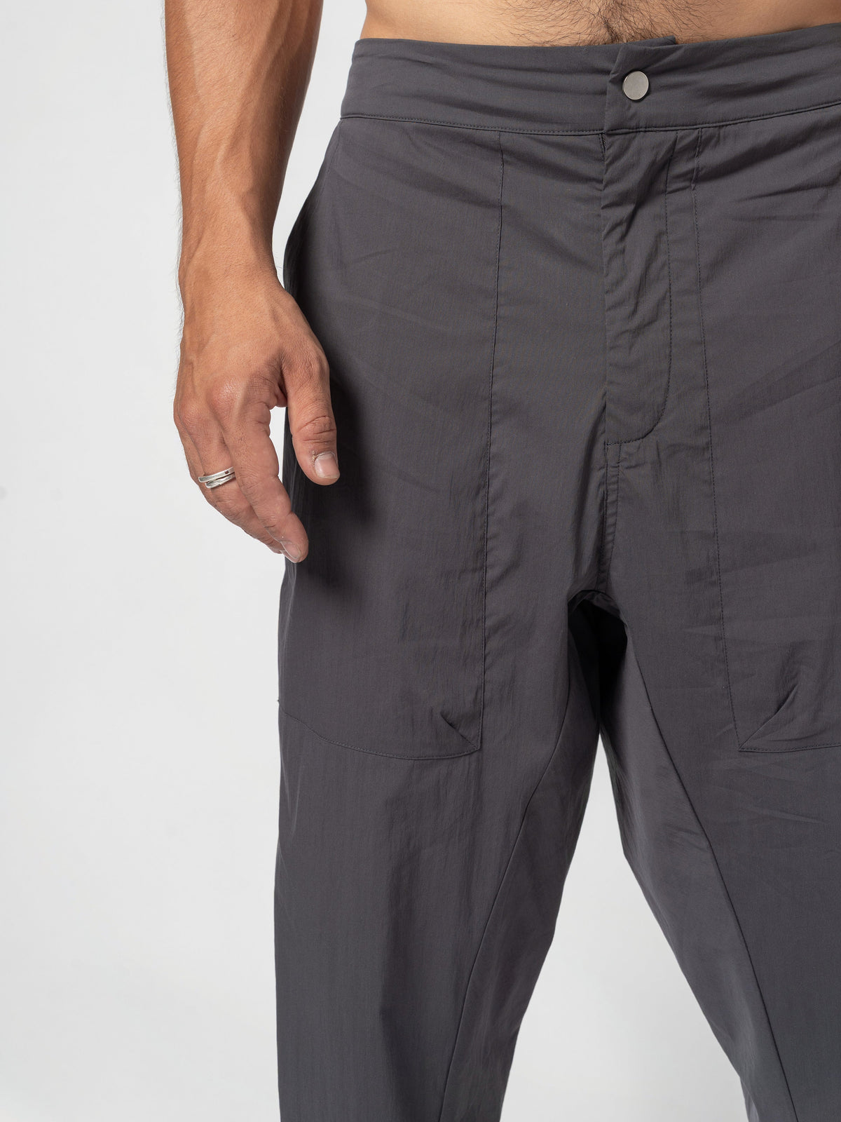 AITO Pleated Drop-Crotch Pants in Dark Grey - close on the waistband and fly, the single button fastened, a hand resting beside it