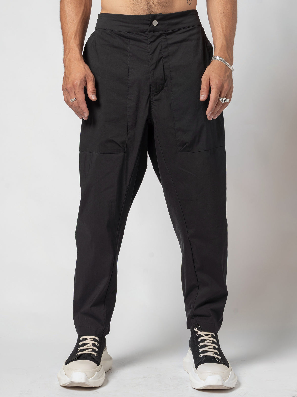 AITO Pleated Drop-Crotch Pants in Black - front view from the waistband down, both arms hanging at the sides, hems breaking over black high-top trainers