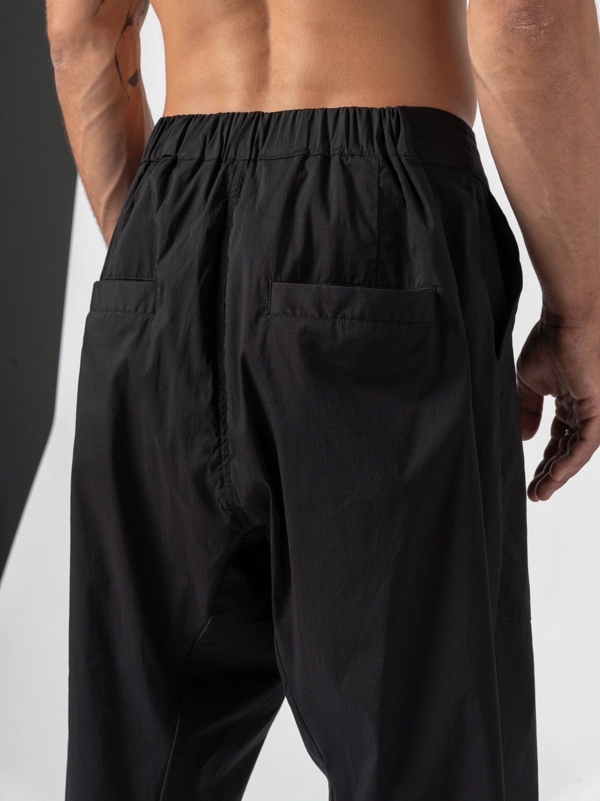 AITO Pleated Drop-Crotch Pants in Black - back close-up with both hands hanging at the edges of the frame, waistband gathers running the full width