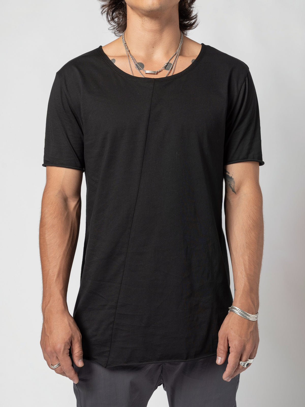 AITO Scoop Neck Cotton T-Shirt in Black - front view of the torso with the weight shifted, the hem hanging lower on one side over the trousers