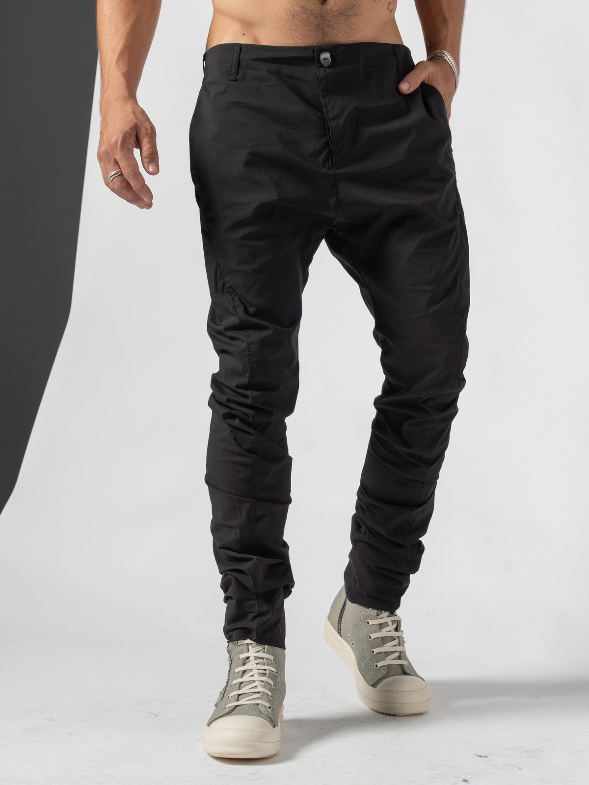 AITO Stacked Hem Slim Pants in Black - front view with both hands in the pockets and one foot set forward